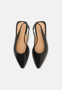 Talons hauts slingback en cuir noir avec des bouts pointus, texture lisse, et une semelle intérieure beige, présentant un design minimaliste et une sangle pour la cheville.
