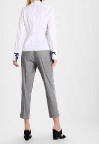 Camisa blanca de manga larga con detalles de cinta azul en los puños, combinada con pantalones cortos de cuadros grises y zapatos negros de tacón cuadrado.