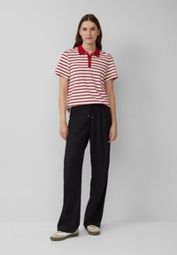 Gestreept poloshirt in wit en rood met een kraag en knoopsluiting, gecombineerd met zwarte, losse broek en casual schoenen.