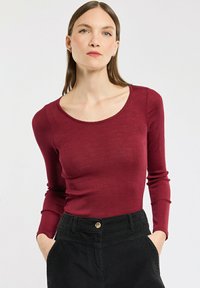 Langärmliges burgunderfarbenes Rippoberteil mit weitem Rundhalsausschnitt, kombiniert mit hoch taillierten schwarzen Cordhosen mit einer knöpfbaren Vorderseite.