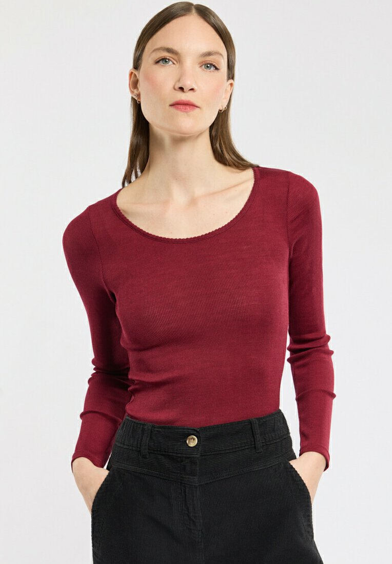 Langärmliges burgunderfarbenes Rippoberteil mit weitem Rundhalsausschnitt, kombiniert mit hoch taillierten schwarzen Cordhosen mit einer knöpfbaren Vorderseite.
