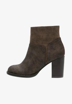 Hnědá semišová kotníková bota s kulatou špičkou, středně vysokým blokovým podpatkem a límcem, který se přehýbá přes horní část boty.