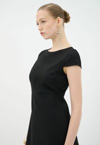 Vestido negro con mangas cortas, parte superior ajustada y falda acampanada. Textura de tela suave, diseño minimalista y escote redondeado.