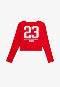 Rode cropped shirt met lange mouwen met witte print "23", "ATHLETIC DEPARTMENT" en "CHICAGO" tekst op de achterkant. Klassieke ronde hals.