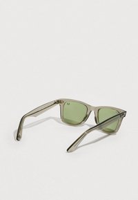 Διαφανή γκρι γυαλιά ηλίου με τετράγωνα πλαίσια, φακούς με πράσινη απόχρωση και λεπτούς βραχίονες με διακριτικό λογότυπο στους ναούς.