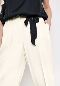 Zwarte top met een vastgebonden strikdetail in de taille, gecombineerd met crèmekleurige wijde broek met voorkeurszakken en een gladde textuur.