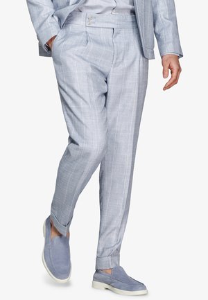 Mann, der hellgraue, kariert Hose mit aufgeschlagenen Säumen und passende blaue Wildleder-Loafer mit weißen Sohlen trägt.