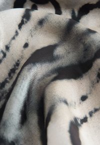 Svilena tkanina s mekanom bež podlogom i crnim apstraktnim uzorcima. Tekstura je glatka s suptilnim sjajem i tekućim padom.