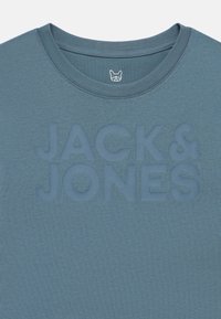 Maglietta blu con scollo a girocollo, con scritta in rilievo "JACK & JONES" e piccolo logo di un cane bianco all'interno del colletto.