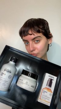 Kit per la cura dei capelli L'Oréal Metal DX con vasetto bianco, bottiglia arancione e dettagli neri, presentato in una confezione nera. Include shampoo, maschera e olio.