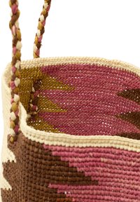 Kudottu kori, joka on valmistettu luonnonkuiduista, sisältää letitetyt kahvat ja geometrisen kuvion vaaleanpunaisen, ruskean ja vihreän sävyissä.