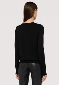 Svart stickad tröja med rund hals och långa ärmar, med smal passform och ribbat nederkant. Matchas med svarta läderbyxor.