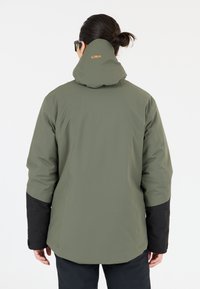 Grøn vandtæt jakke med sorte ærmer, der har en høj krave og CMP-logo på ryggen. Materialet ser glat ud med en mat finish.