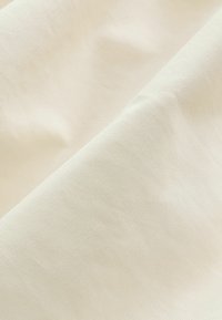 Țesătură albă-crem cu o textură fină, cu bucăți ușor zbârcite. Materialul pare moale și neted, cu un luciu subtil și fără modele.