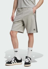 Grijze sportshorts van zachte stof, met zijzakken en zwarte zijkanten. Gecombineerd met zwarte sneakers en witte sokken.
