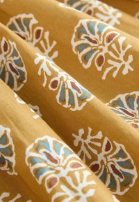 Fabric with a mustard yellow background featuring repeated white and blue floral patterns with brown accents, shown with soft folds.