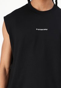 Fekete ujjatlan póló, 100% pamutból készült. Kerek nyakkivágással és fehér "G-STAR RAW" logóval a mellkason. Sima tapintású.