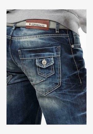 Blauwe denim jeans met een vervaagde afwerking, voorzien van zilverkleurige hardware, decoratieve stiksels en een bruine leren label bij de tailleband.