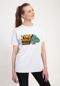 Camiseta blanca de algodón con un dinosaurio de dibujos animados con picos turquesas y un texto en negrita que dice "VIAJERO DEL TIEMPO DE OTRO MUNDO".