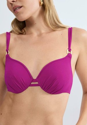 Kobieta w jaskrawym fioletowym bikini z złotymi pierścieniami na ramiączkach, ukazująca górną część tułowia i część twarzy.