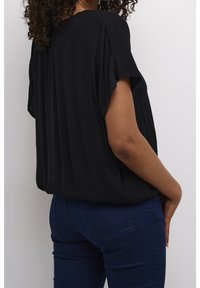 Sort, løstsiddende top med korte ærmer, tekstureret stof og rund halsudskærkning; parret med mørkeblå jeans.