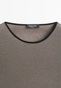 Lichtgrijs katoenen T-shirt met een ronde hals, voorzien van een contrasterende zwarte geribbelde afwerking. Label in het midden van de nek geplaatst.