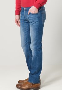 Blå denimjeans med rak benklipp, som har en blekt textur och traditionell femficksdesign, i kombination med bruna ankelstövlar.