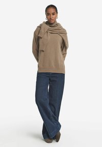 Beiger Pullover mit umgeschlagenem Rollkragen und gerippten Manschetten, kombiniert mit weit geschnittenen dunkelblauen Jeans und taupefarbigen Absatzschuhen.
