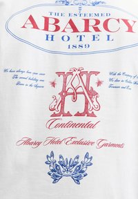 Piros és kék vintage stílusú szöveg és embléma tervezés, amely az "Abarcy Hotel 1889" és a "Continental" feliratokat idézi egy fehér textil hátterén.