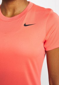 Primer plano de una persona vistiendo una camiseta deportiva Nike de color coral con el logo de swoosh negro de Nike en el pecho.