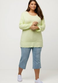 Lys grøn langærmet top med samlede manchetter, sammen med cropped blå jeans og hvide sneakers. Glat stof og afslappet pasform.