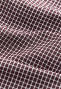 Gros plan sur un tissu bordeaux avec un motif à carreaux blancs et une couture visible traversant horizontalement la surface.