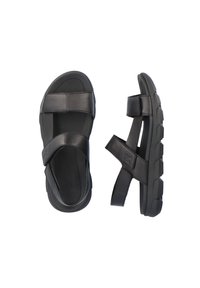 Sandales noires avec semelles plates, larges sangles traversant le pied et la cheville, fabriquées en matériau synthétique avec une finition texturée.