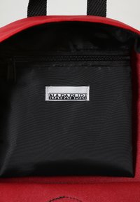 Roter Rucksack-Innenraum mit einer schwarzen Reißverschlusstasche und einem weißen Etikett mit "NAPAPIJRI" auf einem strukturierten Stoff.