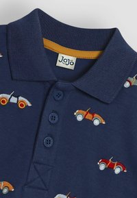 Marineblå polo skjorte med strikket krave og tre knapstolper. Har farverige broderede vintage biler i forskellige farver.