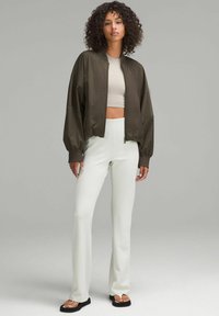 Oliivinvihreä pommijakku, jossa on leveät hihat ja lyhyt malli, yhdistettynä valkoisiin ribattuisiin leveälahkeisiin housuihin ja mustiin tasapohjaisiin sandaaleihin.