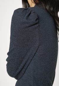 Ciemnoniebieski sweter z bufkami, teksturowanym materiałem, dopasowanym krojem i gładkim wykończeniem. Skupienie na detalach rękawów.