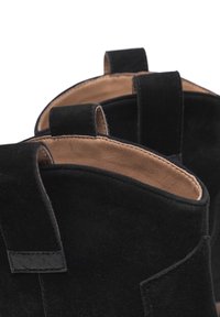 Botas de tobillo de ante en negro con forro de cuero y un interior en contraste color marrón claro. Presentan bucles de tela duales para ponerlas y quitarlas con facilidad.