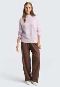 Pulover tricotat de culoare violet deschis, cu un guler înalt, asortat cu pantaloni lejeri maro și adidași albi, creând un aspect relaxat și casual.