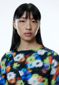 Bunt gemustertes Kleid mit floralen Motiven in Blau, Grün, Orange und Schwarz. Das Material wirkt glatt, mit einer figurbetonten Silhouette und Rundhalsausschnitt.