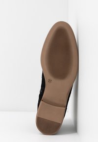 Semelle d'une chaussure noire vue de face, montrant une bande de roulement en caoutchouc brun avec des motifs rainurés et la taille 37 près du talon.