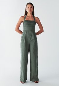 Olijfgroene halternek jumpsuit met geribbelde bovenkant, rechte wijde pijpen en gestructureerde stof. Voorzien van een getailleerde taille en subtiele glans.
