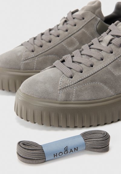 Un paio di sneaker in suede grigio con suole spesse e rigate e un laccio abbinato a spirale etichettato "Hogan" posizionato davanti.