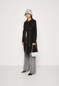 Svart glidelåsdress med krage, parret med grå vide jeans, en rutete bøttehatt og en liten blå mønstrete handveske.