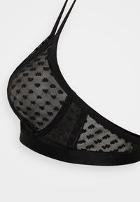 Svart gjennomsiktig mesh-bralette med små hjerteformer, tynne skulderstropper og en bred støttende underdel.