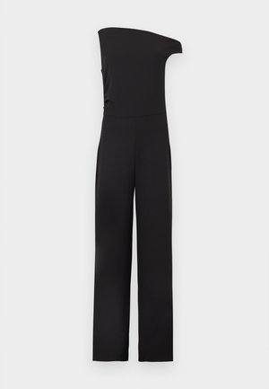 Μαύρη ολόσωμη φόρμα χωρίς μανίκια με σχεδιασμό ενός ώμου και παντελόνι φαρδιάς γραμμής σε απλό φωτεινό φόντο.