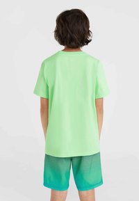 Ljust grön bomulls-T-shirt med korta ärmar, som är kombinerad med teal shorts med ett linjärt gradientmönster och svarta ränder vid fållen.