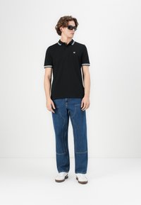 Black polo shirt with white stripes on the collar and sleeves, paired with loose-fitting blue denim jeans and white sneakers.