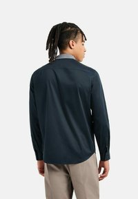 Camicia a maniche lunghe di un blu navy scuro con una texture liscia, un colletto e polsini con bottoni. Presenta un colletto interno con un motivo discreto.