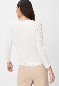 Witte langslieve top met een ronde halslijn, met een naadtoogdetail aan de achterkant. Gepaard met beige broeken, gladde textuur, casual pasvorm.